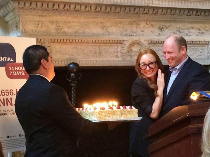 Singer Tori Amos hugs RAINN president Scott Berkowitz. A man presents her with a birthday cake.